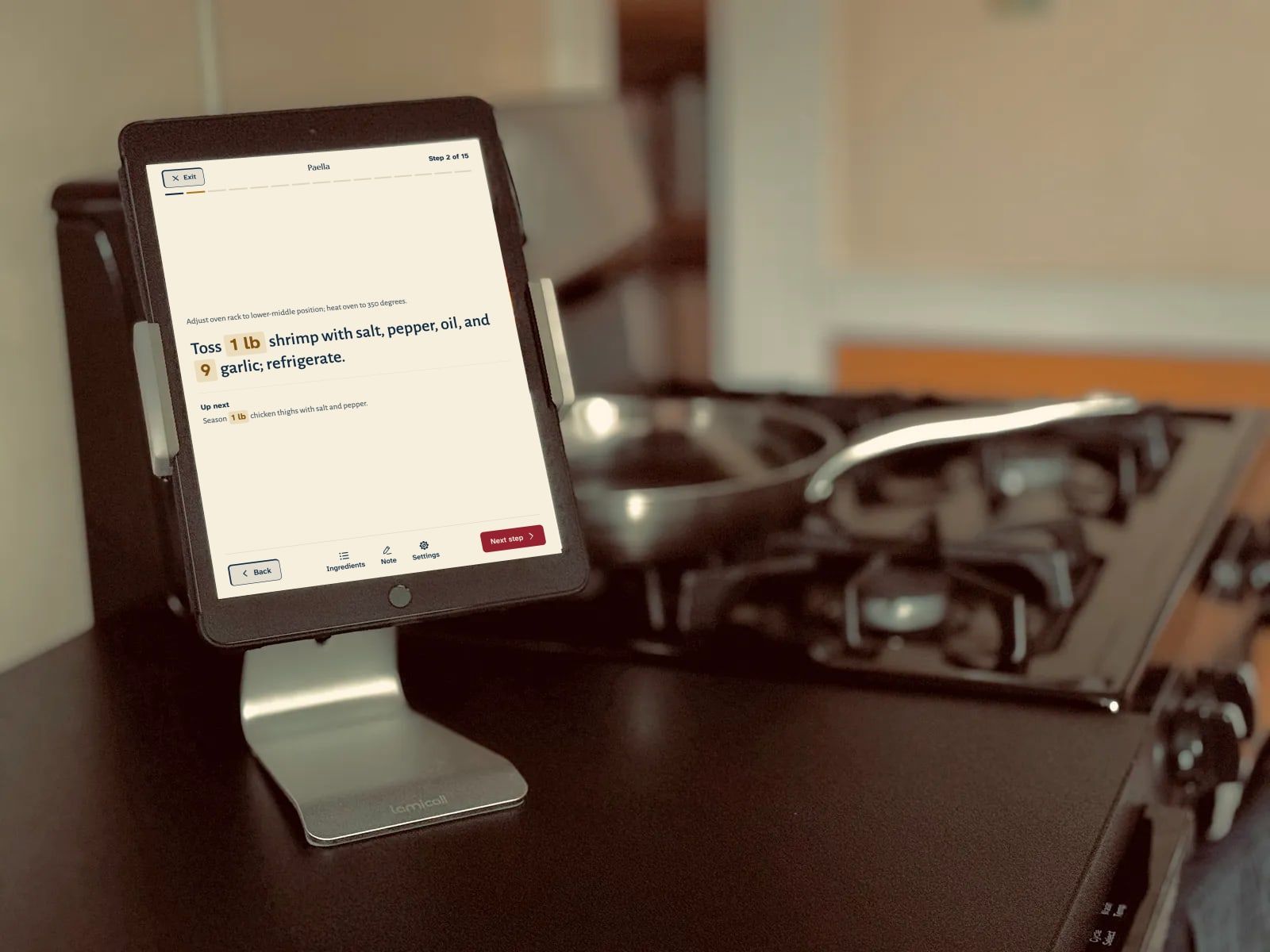 An iPad on a stand beside the stove, open in cooking mode: a step of the paella in large type, with the amounts highlighted
